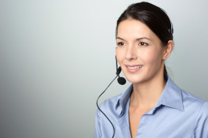 Attractive female call center operator, client services assistant or telemarketer wearing a headset looking at the camera with a charming friendly smile, on grey with copy space