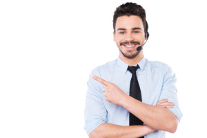 Advertising your product. Handsome young male operator pointing away and smiling while standing against white background
